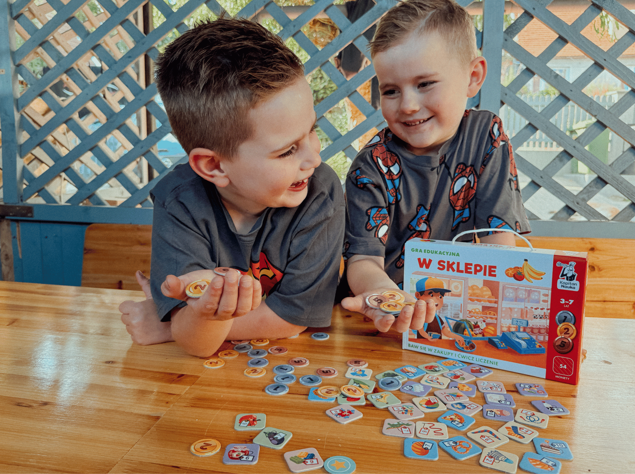 Dwóch chłopców bawi się grą edukacyjną W sklepie, trzymając w dłoniach monety